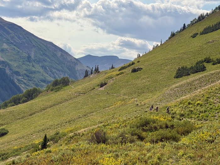 Riders traversing a steep green hillside high above a valley