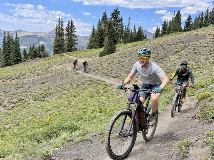 Riders climbing the 401 Trail with conifers and peaks in the background