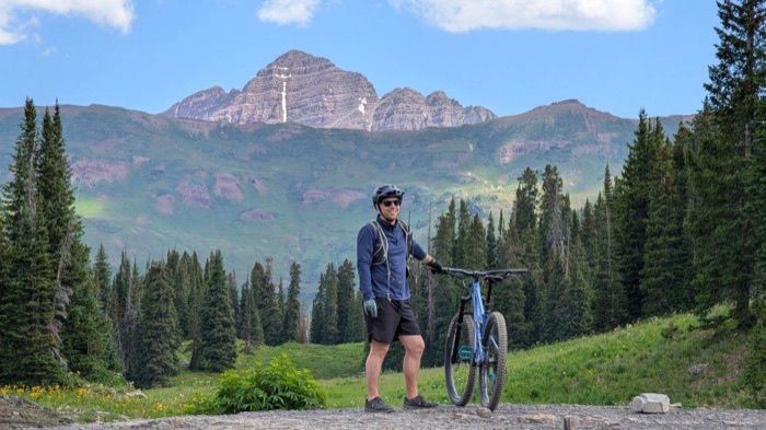 A rider standing with their bike below the Maroon Bells