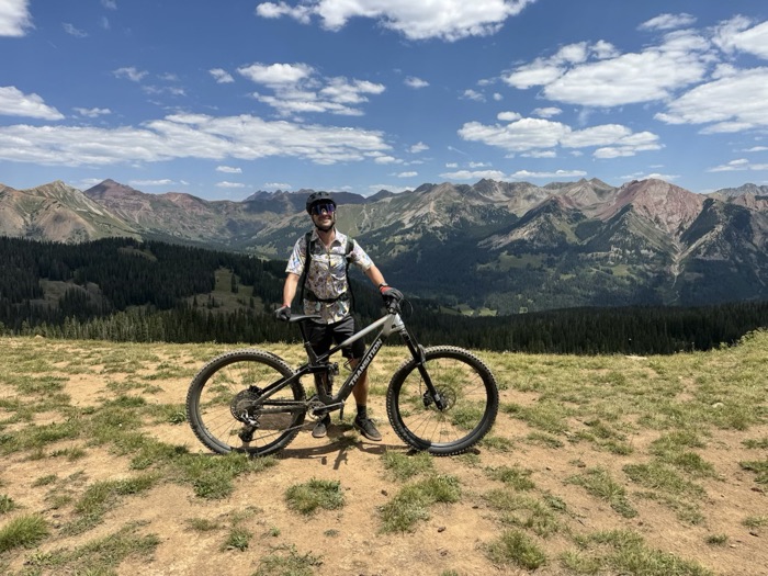 A rider pausing on a high saddle with the Elk Mountains spread out behind