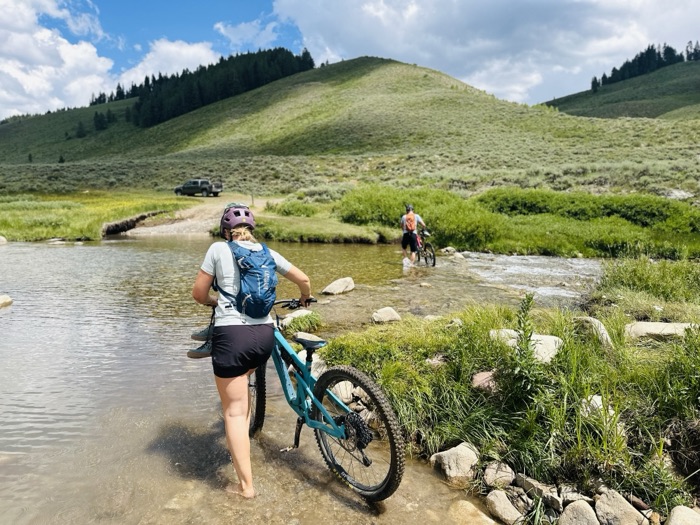 A rider walking a bike across a shallow creek crossing on the Doctor's Park trail