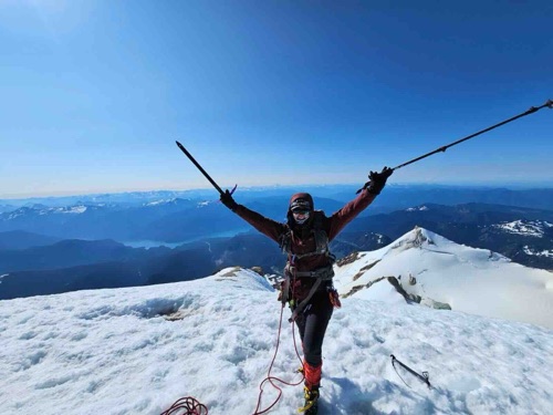 Alexandra Dinello, MD, on a snow-covered summit with ski poles raised