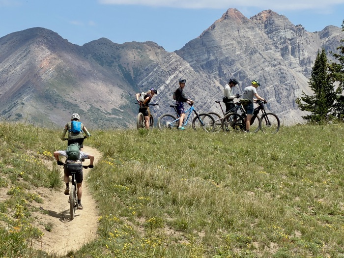 Riders pausing below a jagged ridgeline of layered rock