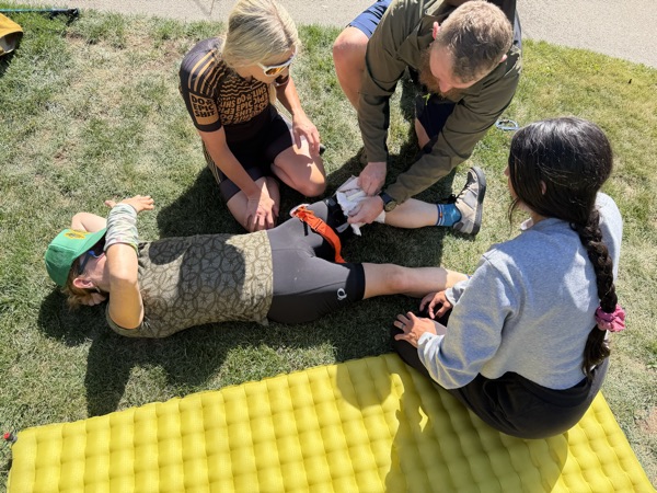 Applying a tourniquet to a simulated leg injury on the ground