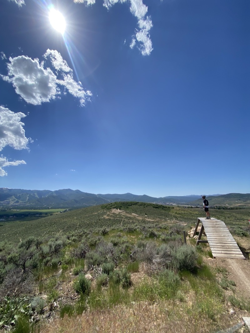 A rider standing at the top of a wooden bike park feature above a wide valley